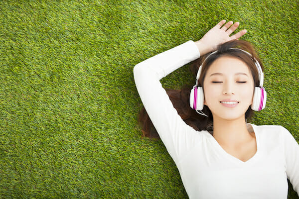 Relaxed woman listening to the music with headphones lying on the grass